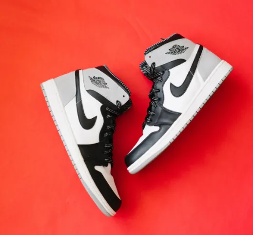 Air Jordan 1 high-top sneakers in grey, white, and black on a red background.
